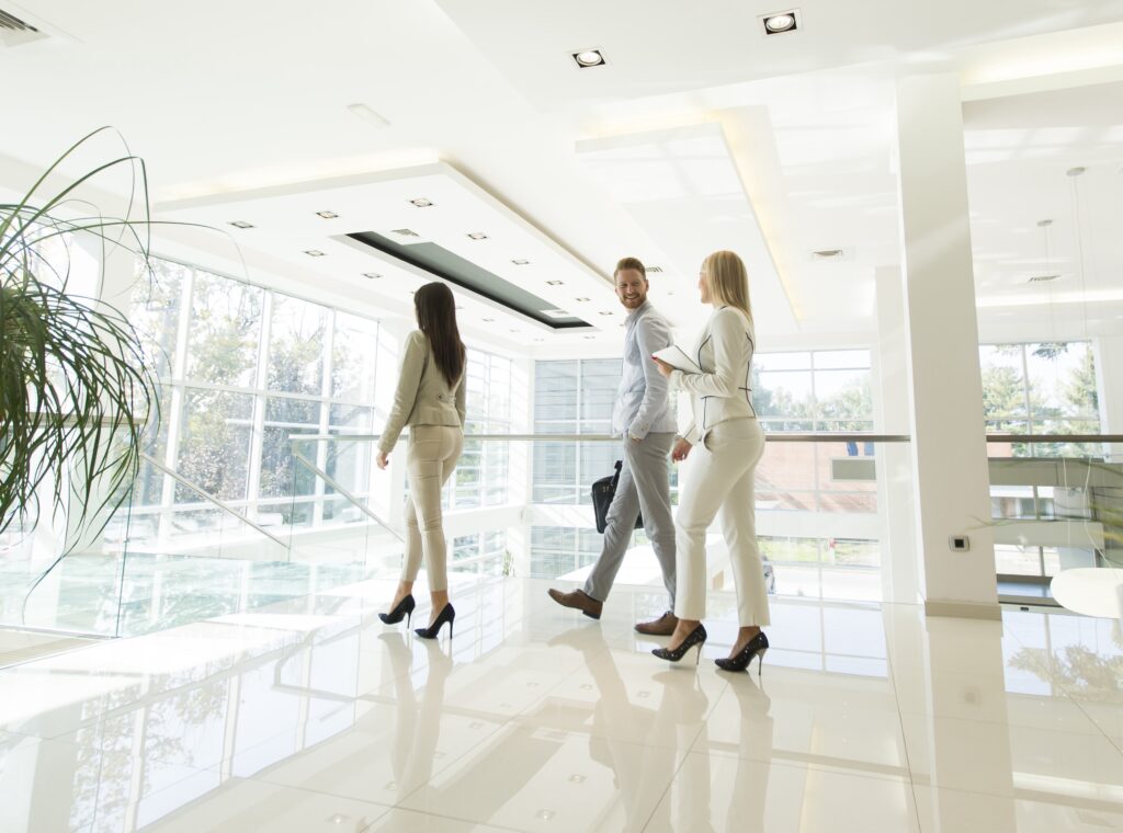 Three professionals walk through a bright, modern office building with glass walls and glossy floors, discussing innovative finance solutions.