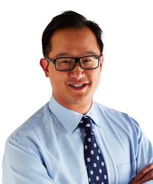 A man in a light blue shirt and dark blue polka dot tie is smiling and wearing glasses, standing against a white background, ready to discuss car loans.