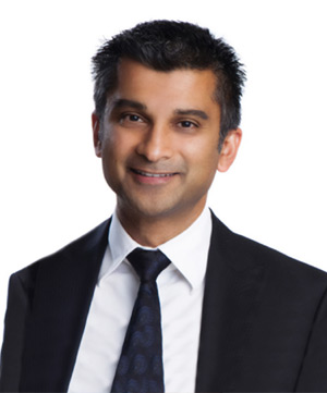 A man with short black hair wearing a black suit, white shirt, and dark tie is smiling in front of a white background, perhaps reflecting on his smooth experience with auto financing.