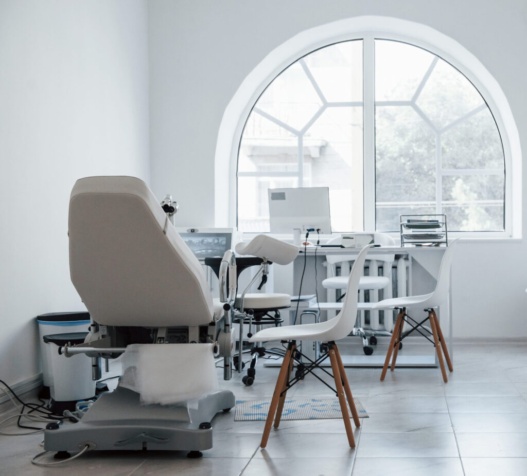 A clean, white dental office with a large arched window, dental chair, and neatly organized desk with chairs, showcasing a professional fit-out designed to maximize comfort and efficiency.