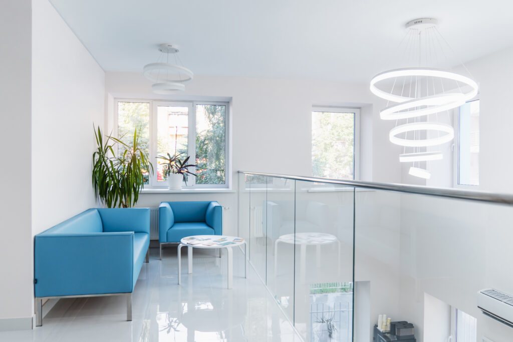 A modern finance-themed waiting area features blue armchairs, a small white table, potted plants, large windows, and circular hanging lights, all thoughtfully chosen in the recent fit-out.