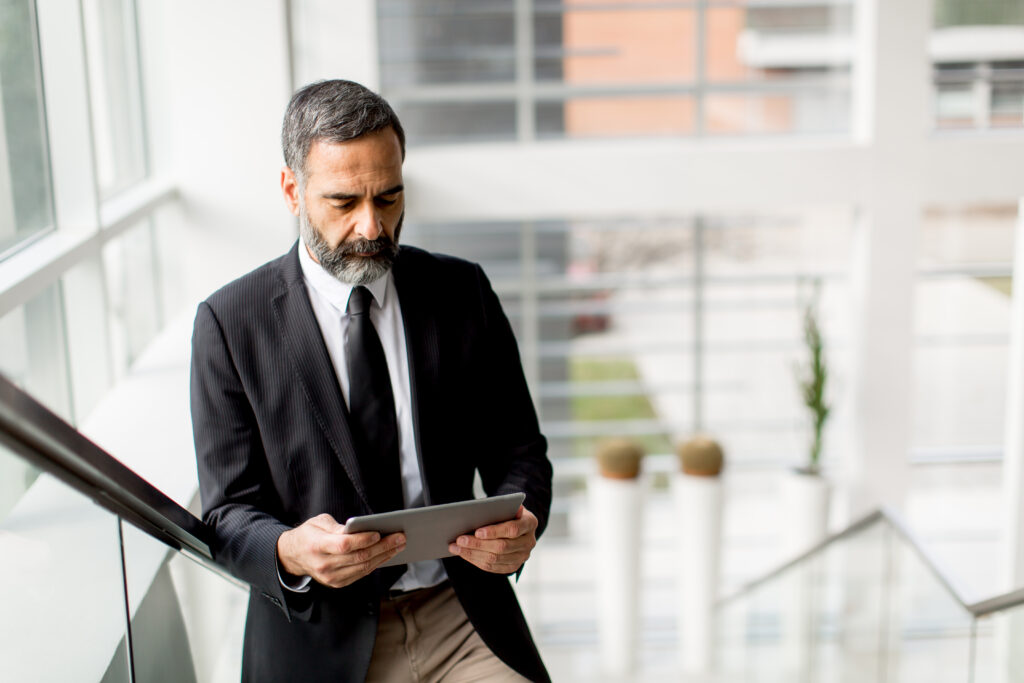 A man in a suit stands by a window holding a tablet, looking at its screen, possibly browsing the help center.