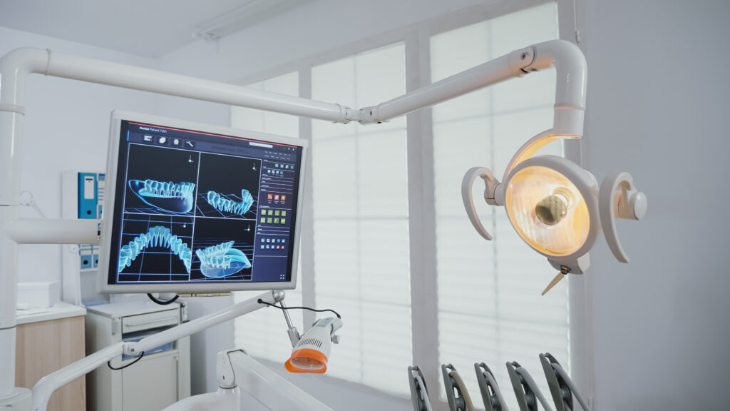 Dental office setup with a monitor displaying dental X-ray images, an overhead dental light, and various equipment financed for optimal patient care in a brightly lit room.